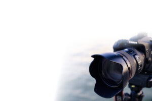 Professional Photographer A close-up of a Canon DSLR camera with a large lens, ideal for Wedding Photography, mounted on a tripod and positioned on the right side against a soft, white gradient background on the left. www.maranonimagery.com