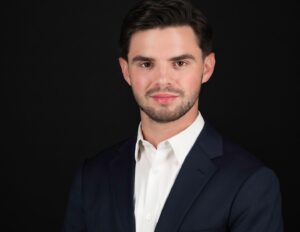 Professional Photographer A young man with short dark hair and a trimmed beard, wearing a white dress shirt and a dark suit jacket, poses confidently for professional headshots against a plain black background, looking directly at the camera. www.maranonimagery.com