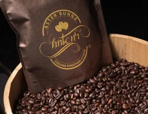 Professional Photographer A bag labeled Aster Bunna Genuine Ethiopian Coffee rests partly inside a wooden container filled with roasted coffee beans, against a dark background—perfect for creative wedding photography or striking portraits. www.maranonimagery.com
