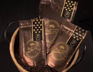 Professional Photographer Four sealed, metallic brown coffee bags labeled Aster Bunna rest in a basket filled with coffee beans. The packaging features gold embossed designs and text, with patterns of yellow flowers—perfect for headshots or creative portraits. www.maranonimagery.com