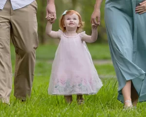 Professional Photographer A young girl in a pale pink dress holds hands with two adults as they walk on green grass. Perfect for wedding photography, the girl looks up, smiling, while the adults’ faces are out of the frame. www.maranonimagery.com