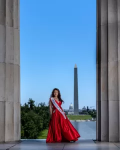 Professional Photographer A woman in a red gown and pageant sash poses for elegant portraits between marble columns at the Lincoln Memorial, with the Washington Monument and U.S. Capitol visible on a clear, sunny day. www.maranonimagery.com