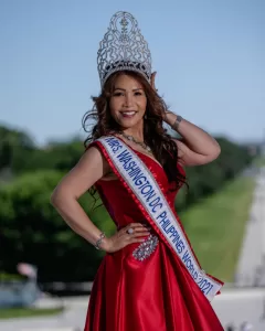 Professional Photographer A woman in a red gown and ornate crown smiles, wearing a sash that reads Mrs. Washington DC Philippines World 2021, captured by the photographer with a blurred outdoor background and green trees behind her. www.maranonimagery.com