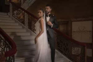 Professional Photographer A bride in a white gown and a groom in a black tuxedo stand together on an elegant staircase with ornate railings, posing for a formal wedding photography portrait by a professional photographer. www.maranonimagery.com