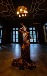 Professional Photographer A woman in a long, elegant bronze gown and layered pearl necklaces poses dramatically in a dimly lit, ornate room—a captivating scene worthy of any wedding photography portfolio or skilled photographer’s portraits. www.maranonimagery.com