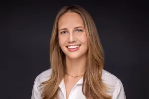 Professional Photographer A woman with long light brown hair, wearing a white shirt and a simple gold necklace, smiles at the camera against a dark background—an elegant example of natural headshots. www.maranonimagery.com