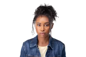 Professional Photographer A young woman with curly hair tied up, wearing a denim jacket over a light shirt, looks directly at the camera with a serious expression against a white background—perfect for professional headshots or portraits by any skilled photographer. www.maranonimagery.com