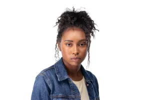 Professional Photographer A young woman with curly hair in a puff hairstyle wears a denim jacket over a light shirt and looks directly at the camera with a neutral expression, against a white background—perfect for modern portraits. www.maranonimagery.com