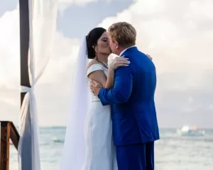 Professional Photographer A bride in a white dress and veil kisses a groom in a blue suit outdoors by the water, with boats and clouds in the background, capturing a dreamy portrait reminiscent of timeless headshots. www.maranonimagery.com