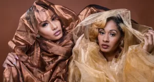 Professional Photographer Two women pose closely together for the photographer, partly wrapped in sheer, shiny fabrics—one in copper brown, the other in gold. They gaze directly at the camera against a matching brown background, creating striking portraits. www.maranonimagery.com