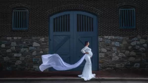 Professional Photographer A pregnant woman in a long white dress stands in front of a large blue wooden door and stone wall, her sheer train flowing dramatically behind her—a stunning moment captured by a talented photographer specializing in portraits and wedding photography. www.maranonimagery.com
