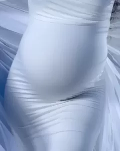 Professional Photographer A close-up of a pregnant belly covered by a form-fitting white dress, with soft fabric folds and flowing material visible in the background—perfect inspiration for elegant maternity or wedding photography. www.maranonimagery.com