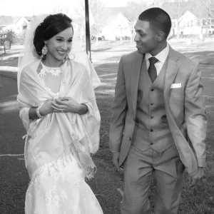 Professional Photographer A bride in a white lace dress and a groom in a light suit walk side by side outdoors, smiling at each other on their wedding day—an enchanting moment perfect for timeless portraits. www.maranonimagery.com