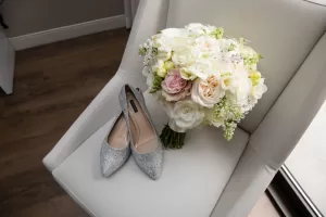 Professional Photographer A pair of glittery silver flats and a bouquet of white and pale pink flowers rest on a white cushioned chair near a window—an elegant scene perfect for wedding photography. www.maranonimagery.com