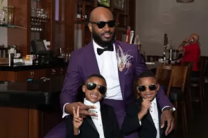Professional Photographer A man in a purple suit and sunglasses sits in a restaurant with two young boys in black tuxedos and sunglasses, both smiling and making peace signs—like a scene from trendy wedding photography or playful family portraits. www.maranonimagery.com