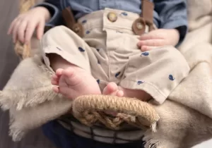Professional Photographer A close-up portrait of a young child sitting on a blanket, showing their bare feet and legs in beige pants with blue whale prints and brown suspenders. The child’s upper body and face are out of focus. www.maranonimagery.com