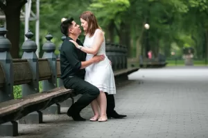 Professional Photographer A couple shares an intimate moment on a park bench. The photographer captures the man in black as he sits, gazing into his partner's eyes. Surrounded by trees and greenery, this portrait radiates romance and tranquility. www.maranonimagery.com