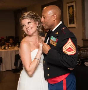 Professional Photographer A bride in a white dress and a groom in a decorated military uniform share a joyful dance at their wedding reception—captured through elegant wedding photography—as they smile and look happy together. www.maranonimagery.com