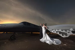 Professional Photographer A bride and groom stand in front of a private jet at sunset. The bride’s flowing veil and the groom’s dark suit are beautifully captured, showcasing romantic wedding photography with an elegant, dramatic atmosphere. www.maranonimagery.com