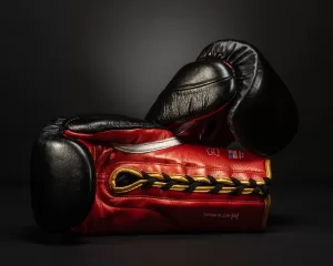 Professional Photographer A pair of red and black boxing gloves with gold laces rest against each other on a dark background, captured in a striking portrait style. www.maranonimagery.com