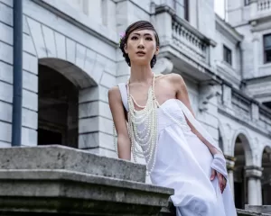 Professional Photographer A woman in a white strapless dress and layered pearl necklaces stands outside a grand stone building, gazing thoughtfully into the distance—a perfect moment for timeless wedding photography portraits by an expert photographer. www.maranonimagery.com