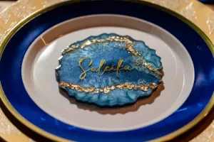 Professional Photographer A place setting with a white plate bordered in blue and gold holds a decorative, blue resin coaster with gold accents and the word Sulcifa in gold cursive—a perfect backdrop for pet photography or creative portraits. www.maranonimagery.com