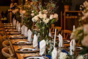 Professional Photographer A long, elegant dining table is set with white napkins, silver-rimmed plates, and tall floral centerpieces featuring roses and greenery—perfect for capturing stunning wedding photography in a festive, sophisticated atmosphere. www.maranonimagery.com