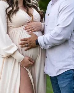 Professional Photographer A couple stands close together; the woman in a cream dress cradles her pregnant belly while the man places his hand gently over hers, both showing wedding rings. This intimate wedding photography portrait captures a tender, expectant moment. www.maranonimagery.com
