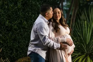 Professional Photographer A photographer captures a man gently kissing a pregnant woman on the forehead as he cradles her belly. Surrounded by greenery, they share an affectionate and tender moment in this beautifully composed outdoor shot. www.maranonimagery.com