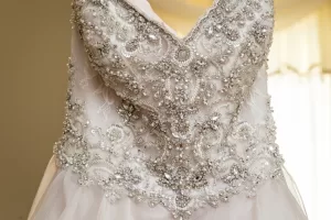 Professional Photographer Close-up of a white wedding dress bodice decorated with intricate beadwork, sequins, and lace embroidery, creating an ornate, elegant pattern—perfect for wedding photography. The background is softly lit and out of focus. www.maranonimagery.com