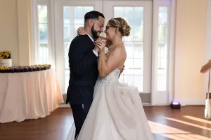 Professional Photographer A bride and groom share a joyful first dance in a bright room with large windows behind them. Captured through timeless wedding photography, they smile and hold hands, gazing into each other’s eyes. www.maranonimagery.com