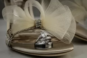 Professional Photographer A close-up of elegant, rhinestone-embellished high-heeled shoes with a large mesh bow, featuring a stack of three wedding rings placed on the toe—captured by a photographer with an eye for stunning portraits. www.maranonimagery.com