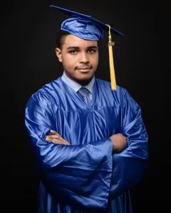 Professional Photographer A young man in a blue graduation gown and cap with a gold tassel stands with his arms crossed, looking at the camera against a black background—perfect for showcasing a photographer's portrait skills. www.maranonimagery.com