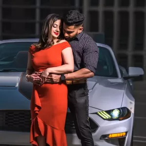 Professional Photographer A couple poses in front of a silver car at night in this striking portrait. The woman, in a red dress, stands up front while the man, dressed in black, embraces her from behind. Their happy, affectionate expressions showcase the photographer's skill. www.maranonimagery.com