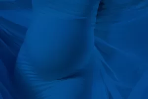 Professional Photographer A close-up of a pregnant belly wrapped in sheer, flowing blue fabric, captured by a skilled photographer, creating soft folds and a sense of gentle movement. www.maranonimagery.com