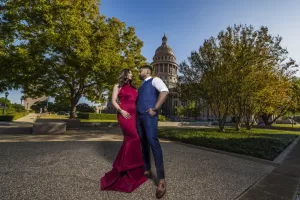 Professional Photographer A couple poses outdoors in formal attire for wedding photography; the woman wears a fitted red dress, and the man dons a navy blue vest and pants. They stand close, gazing at each other, with trees and a domed government building behind them. www.maranonimagery.com