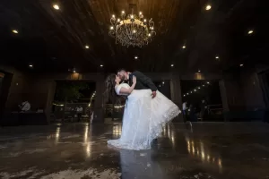 Professional Photographer A bride and groom share a romantic dance under a chandelier in a dimly lit, elegant hall, captured perfectly by a wedding photographer. The groom dips the bride, who wears a white gown, as they kiss on the reflective floor. www.maranonimagery.com