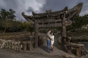 Professional Photographer A couple stands closely together under a rustic wooden archway labeled Entrance to Chinese Tea Garden, surrounded by trees and stone landscaping on a cloudy day, perfectly captured by a skilled wedding photography photographer. www.maranonimagery.com