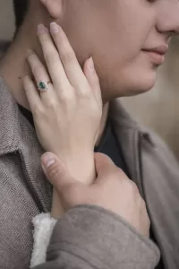 Professional Photographer A close-up portrait of a couple embracing, focusing on their hands. One person wears a ring with a green gemstone, their hand resting gently on the other’s neck, while the other lightly holds their wrist. www.maranonimagery.com