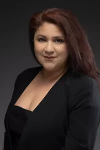Professional Photographer A woman with long, dark reddish-brown hair and light skin is wearing a black blazer over a black top, posing confidently for headshots against a dark gray background. www.maranonimagery.com