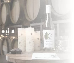 Professional Photographer A bottle of white wine, two glasses, chocolates, candles, and a menu are arranged on a wooden table in front of stacked wine barrels in a softly lit cellar—an inviting scene for any photographer specializing in portraits. www.maranonimagery.com