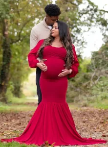 Professional Photographer A photographer captures a pregnant woman in a long, fitted red dress on a leafy path as a man embraces her from behind and kisses her head. They are surrounded by lush greenery and trees, creating a beautiful portrait. www.maranonimagery.com