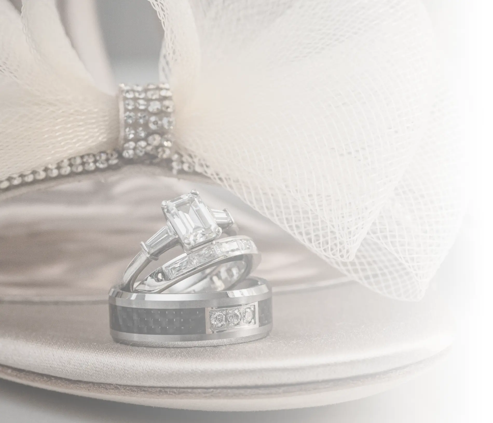 Professional Photographer Three silver rings, including a diamond engagement ring, rest on a satin high-heeled shoe with a jeweled strap and mesh bow, beautifully captured by a professional photographer in soft, light tones. www.maranonimagery.com
