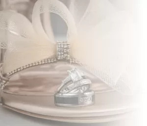 Professional Photographer Three silver rings, including an engagement ring with a prominent gemstone, rest on a high-heeled shoe adorned with a mesh bow and rhinestones—captured in soft, romantic lighting perfect for wedding photography. www.maranonimagery.com
