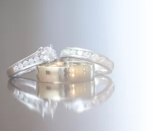 Professional Photographer Three rings—two silver diamond bands and one plain gold band—rest on a reflective surface with a soft, light gradient background, capturing the elegance often sought in wedding photography. www.maranonimagery.com