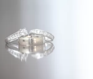 Professional Photographer Three wedding rings—two with embedded diamonds and one plain—are elegantly arranged on a shiny, reflective surface with a soft gradient light background, capturing the timeless beauty often sought in wedding photography. www.maranonimagery.com