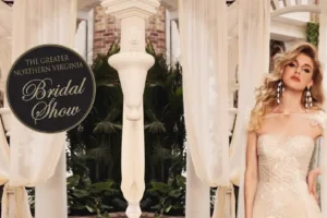 Professional Photographer A woman in an elegant lace wedding dress stands beside cream-colored pillars and draped curtains. Next to her is a circular sign that reads The Greater Northern Virginia Bridal Show, perfect for a photographer specializing in portraits to capture unforgettable moments. www.maranonimagery.com