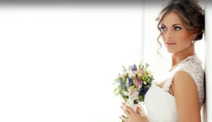 Professional Photographer A bride in a white lace wedding dress holds a colorful bouquet of flowers and gazes thoughtfully out of a bright window, captured beautifully by a skilled photographer known for stunning portraits. www.maranonimagery.com
