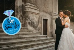Professional Photographer A bride and groom embrace, smiling, on stone steps outside a historic building. On the left, a blue graphic with a diamond reads She Said Yes Wedding Expo—perfect for portraits, pet photography, and headshots. www.maranonimagery.com