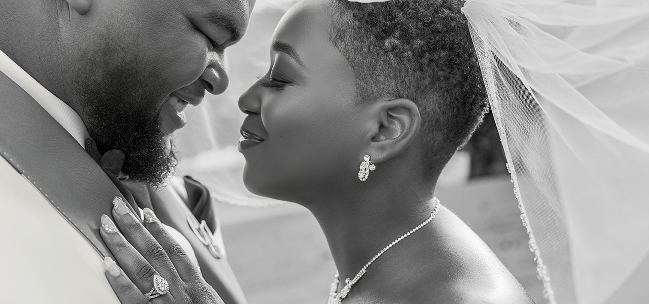 Professional Photographer A close-up black-and-white photo by a wedding photographer of a bride and groom smiling lovingly at each other. The bride wears a veil, earrings, and a necklace, gently touching the groom’s chest as they share an intimate, joyful moment. www.maranonimagery.com